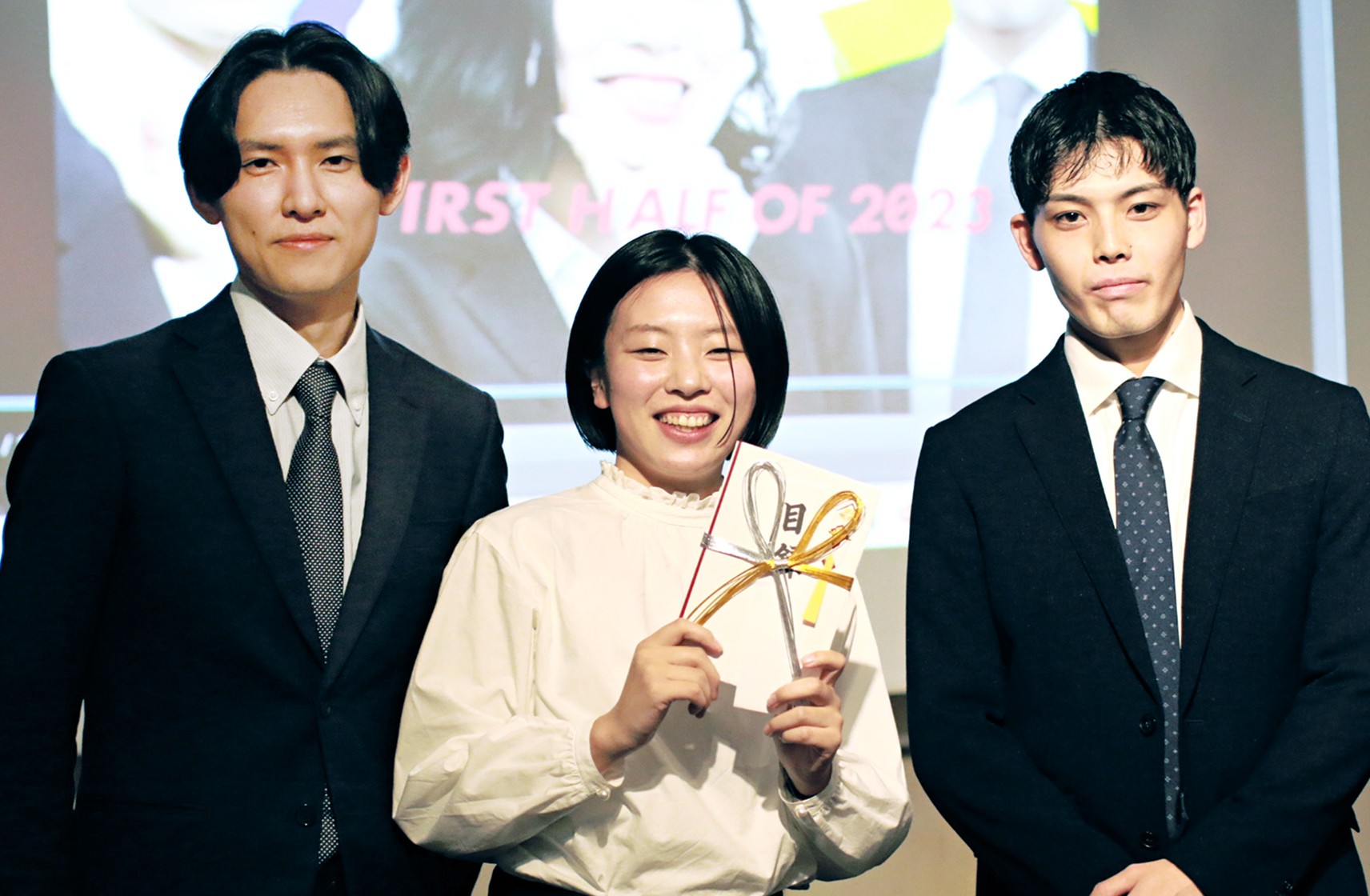 GRAND DESIGNで実施されるCRAZY AWARDで表彰されている笑顔の女性と、2人の男性