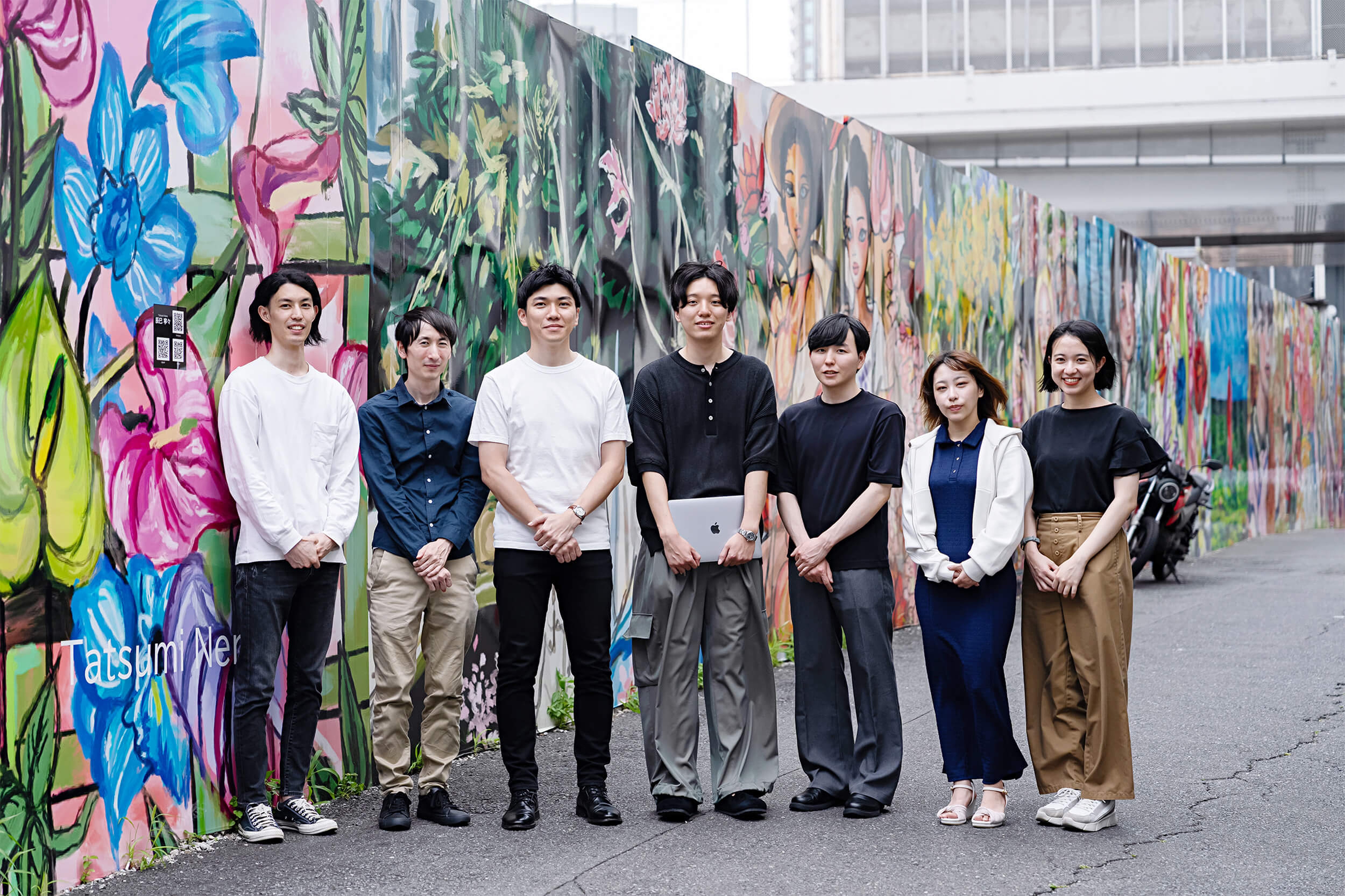 BRANU株式会社で働くメンバーの集合写真。中央の男性はMacBookを手に持っている